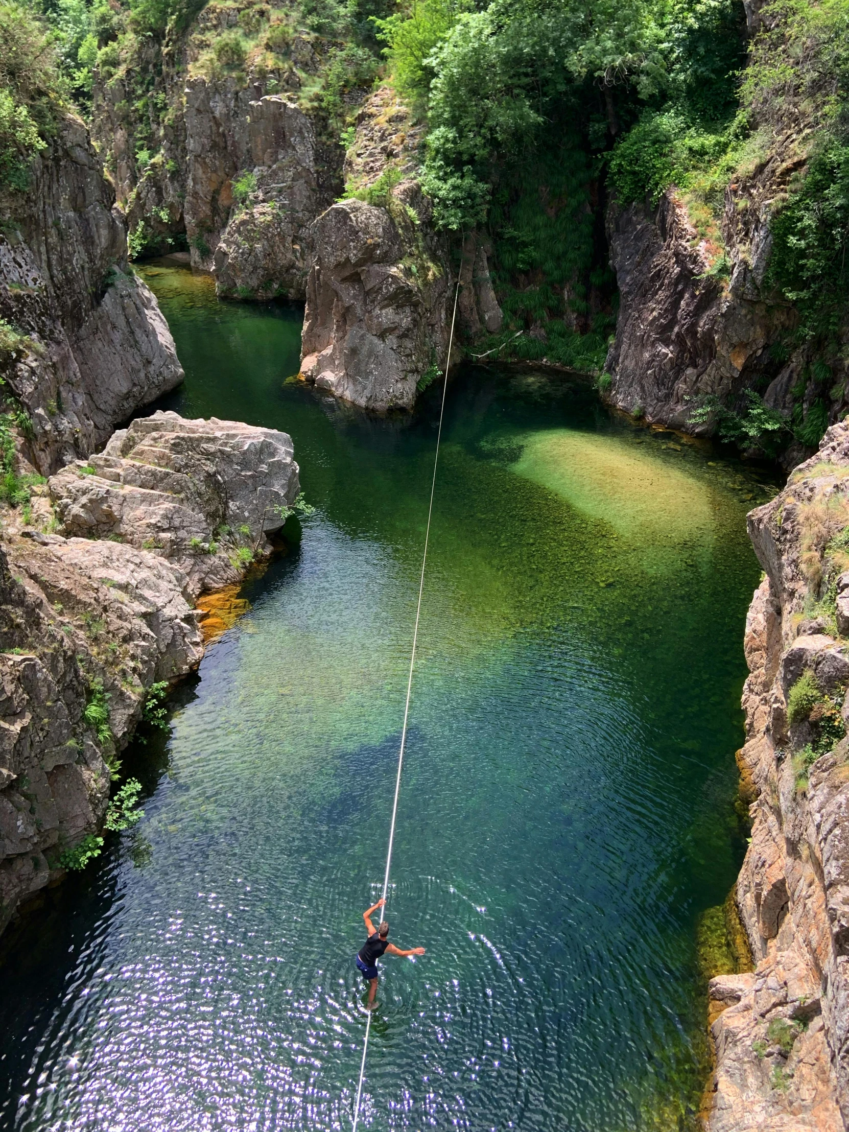 a person on a rope in the middle of a river, lush green, rock pools, head straight down, taras susak