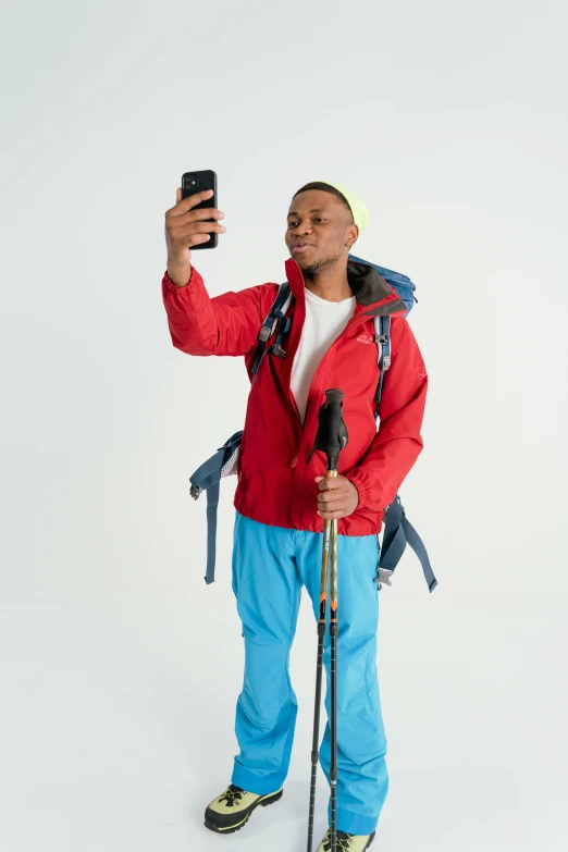 a man taking a selfie with a cell phone, hiking clothes, red and blue garments, ( ( dark skin ) ), full body with costume