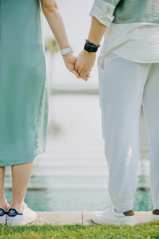 a couple holding hands in front of a body of water, sea - green and white clothes, curated collections, lesbian, wealthy women