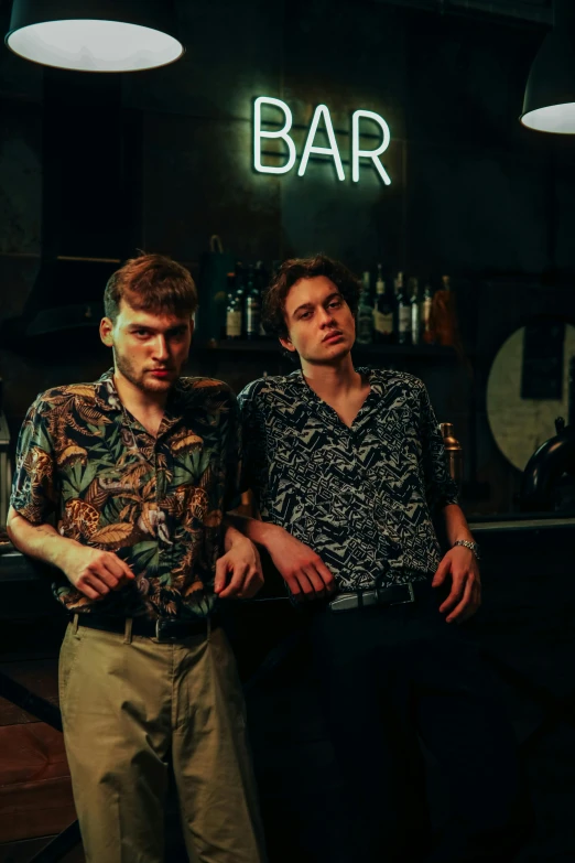 two men standing next to each other in front of a bar, an album cover, by Dicky Doyle, unsplash, renaissance, cute boys, serious faces, large tall, looking partly to the left