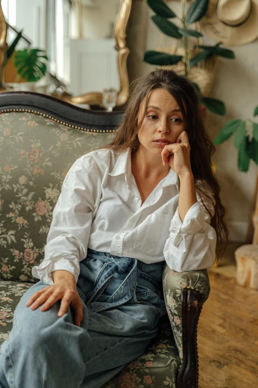 a woman sitting on a couch in a living room, by Adam Marczyński, pexels contest winner, rococo, white shirt and jeans, looking serious, ukrainian, oona chaplin