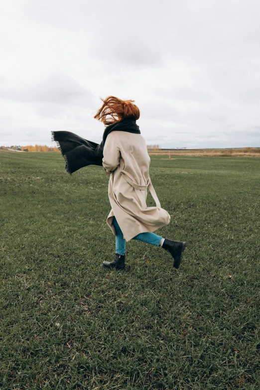 a woman walking across a lush green field, pexels contest winner, cool tousled hair, coat, young redhead girl in motion, winter season