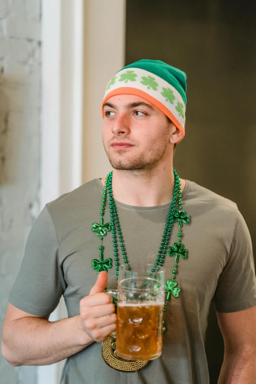 a man in a green hat holding a glass of beer, by Pamela Drew, trending on reddit, irish, wearing several pendants, ethan klein, beads