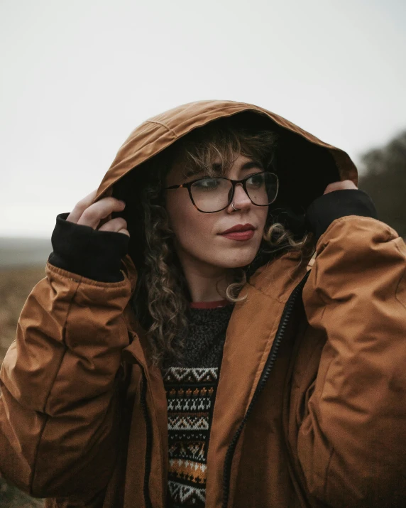 a woman wearing glasses and a brown jacket, inspired by Elsa Bleda, trending on pexels, visual art, grey skies with two rainbows, beautiful nordic woman, wearing adventuring gear, cosy vibes