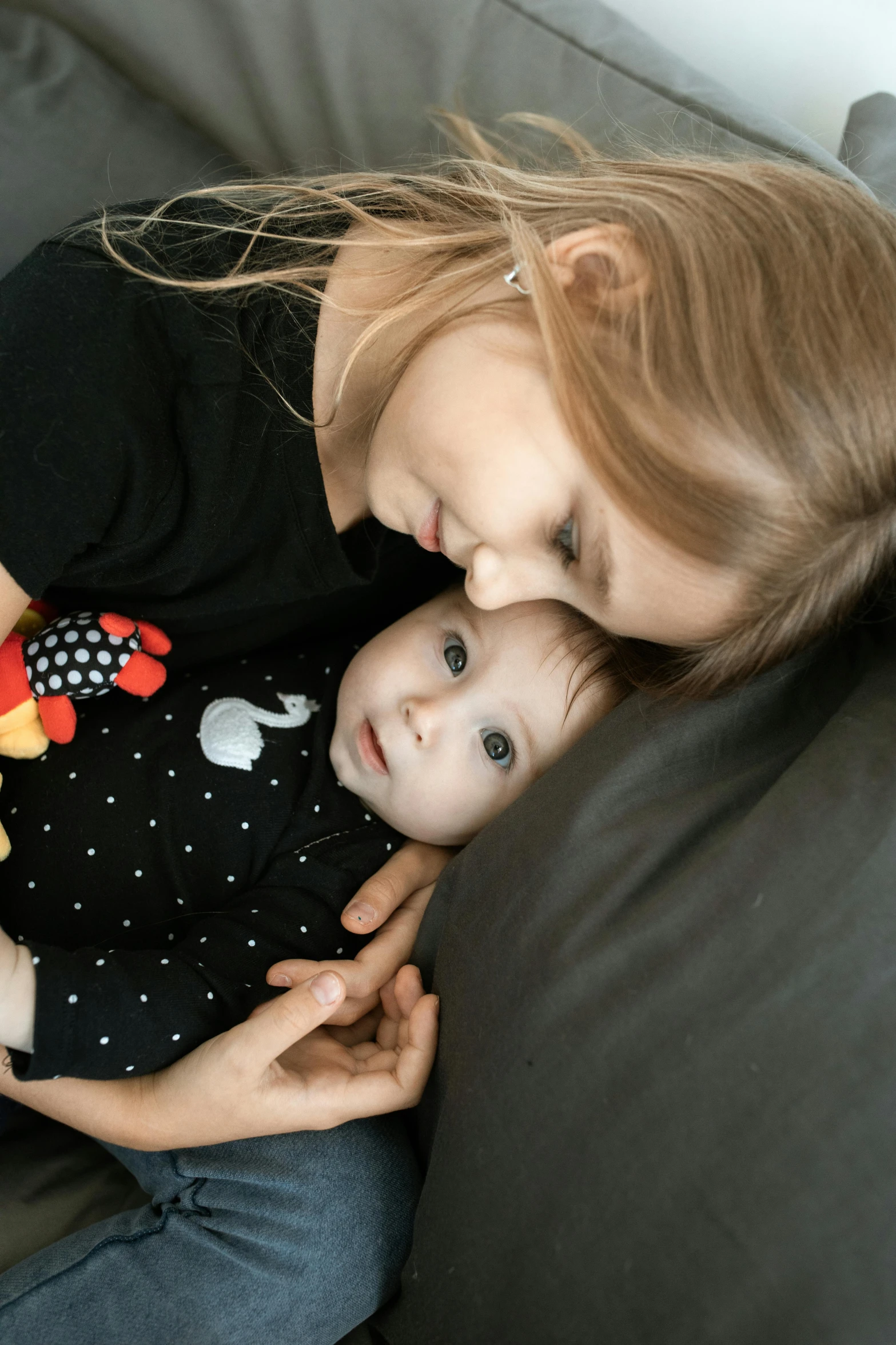 a woman sitting on a couch holding a baby, inspired by Sophie Anderson, trending on reddit, portrait photo, square, black, close - up photograph