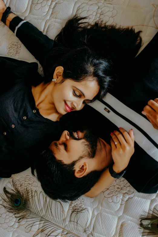 a man and a woman laying on top of a bed, an album cover, pexels contest winner, indian, wearing a black shirt, holding each other hands, looking to his side