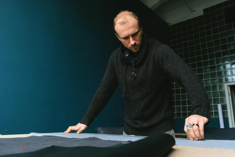 a man is cutting fabric on a table, a portrait, unsplash, wearing dark maritime clothing, blue print, black leather garment, tuomas korpi and wlop