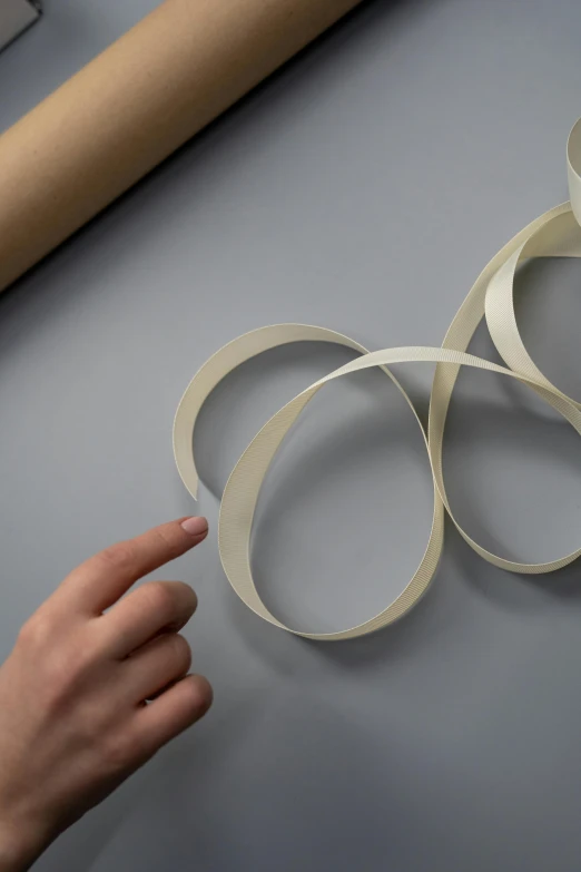 a person holding a piece of paper next to a roll of paper, an abstract sculpture, white ribbon, generative design, silver，ivory, orbital rings