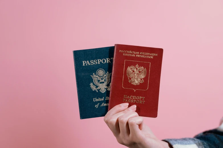 a person holding two passports in their hands, an album cover, by Julia Pishtar, trending on unsplash, pink and red color style, vertical orientation, various posed, dezeen
