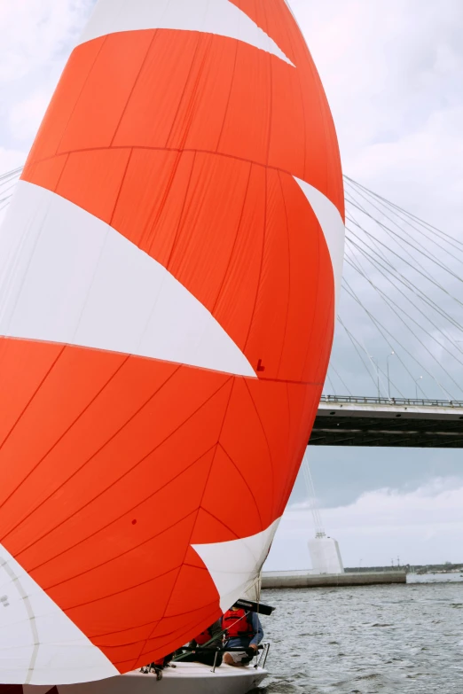 a red and white sailboat with a bridge in the background, inspired by Alexander Stirling Calder, unsplash, happening, orange, sport, detail structure, silks