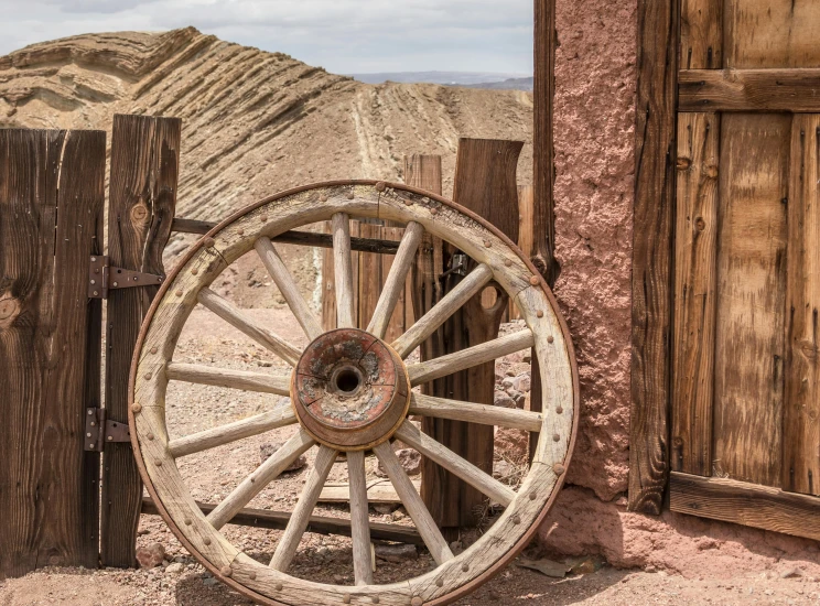 an old wagon wheel leaning against a wooden fence, by Thomas Carr, pexels contest winner, renaissance, ancient ruins under the desert, mining, background image, circular gate in a white wall