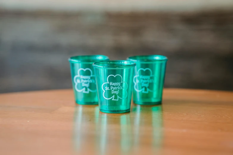 three shot glasses sitting on top of a wooden table, metalic green, clover, product image, fan favorite