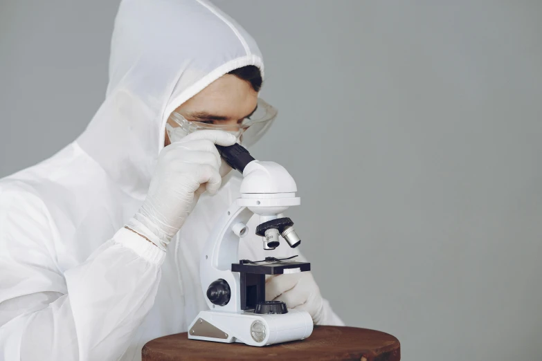a man in a white lab coat looking through a microscope, inspired by Allan Ramsay, pexels contest winner, analytical art, wearing hoods, porcelain organic tissue, woman, white helmet