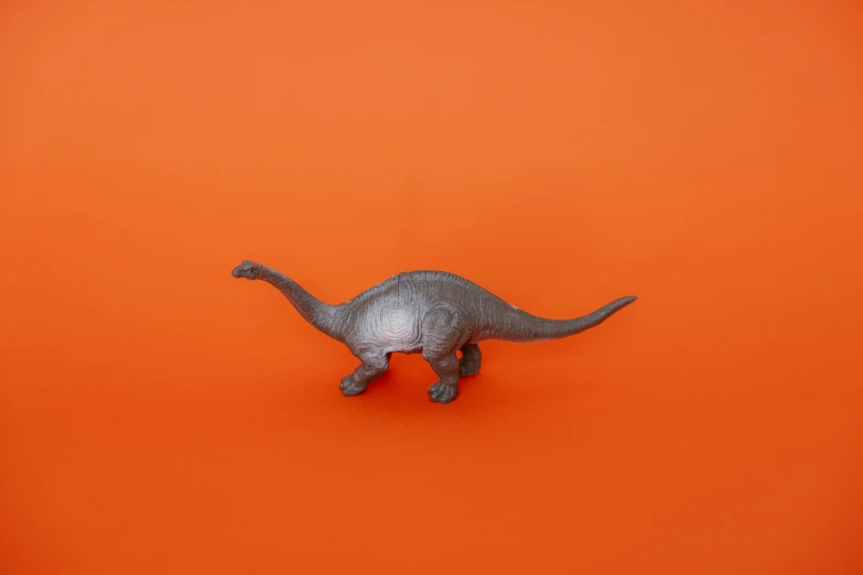 a toy dinosaur on an orange background, by Paul Bird, trending on unsplash, magic realism, ffffound, grey, hyperrealistic simulation, metal tail