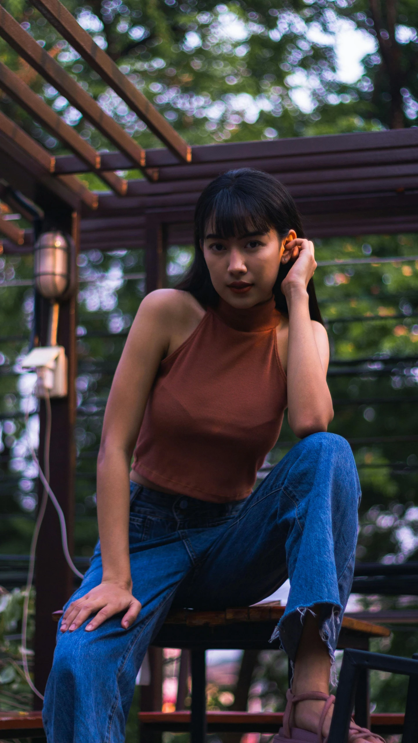 a woman sitting on a bench talking on a cell phone, an album cover, inspired by Elsa Bleda, trending on pexels, realism, sleeveless turtleneck, asian girl, croptop, a 35mm photo