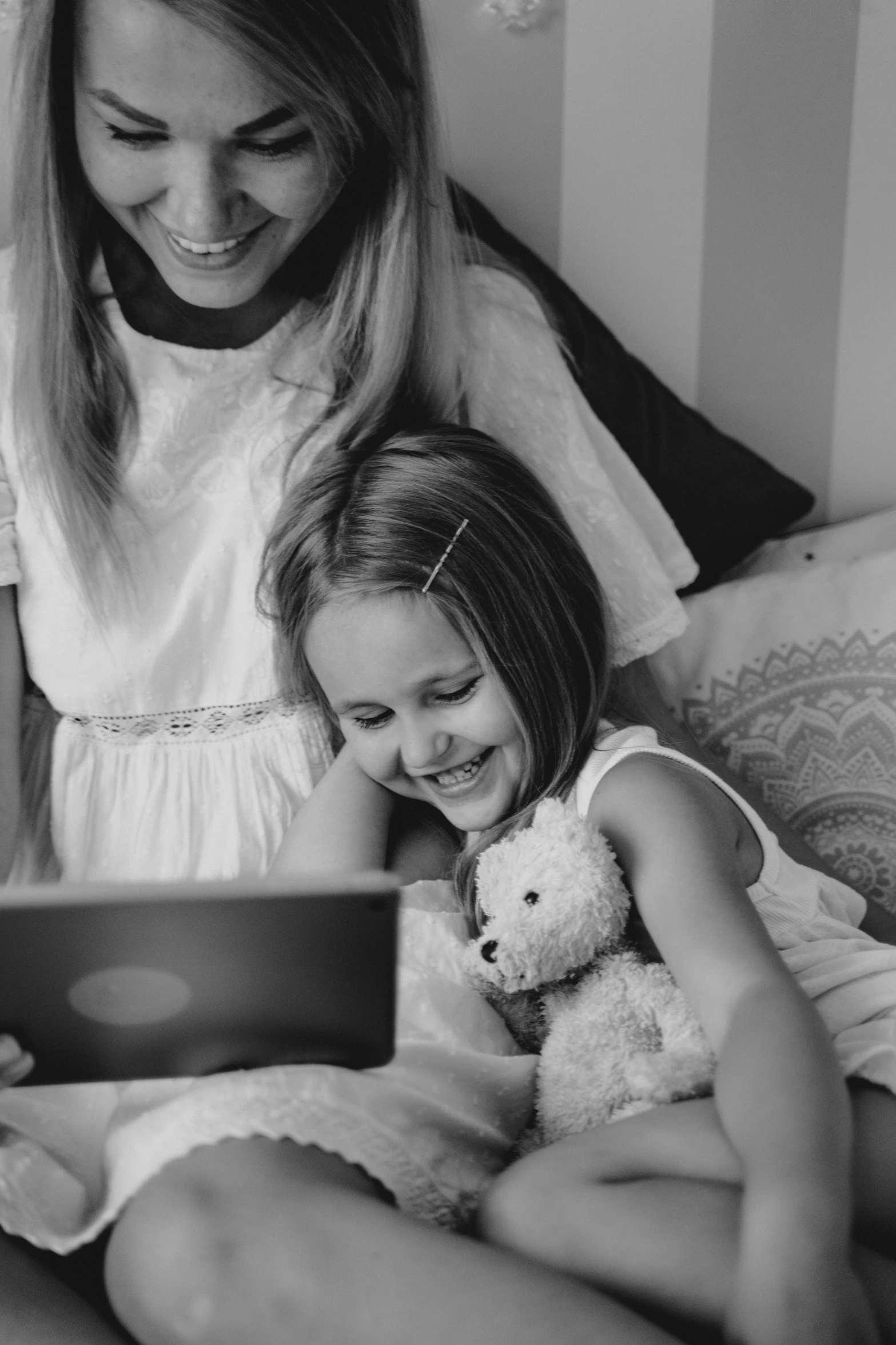 a woman sitting next to a little girl on a bed, a black and white photo, pexels, integrating with technology!!, 🎀 🍓 🧚, friends, reading