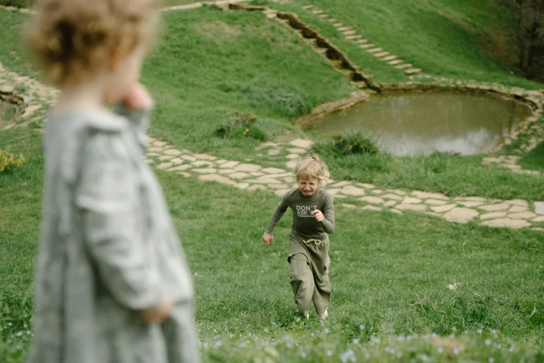 a little boy that is standing in the grass, inspired by Kate Greenaway, pexels contest winner, be running up that hill, medium shot of two characters, terraced orchards and ponds, running towards camera