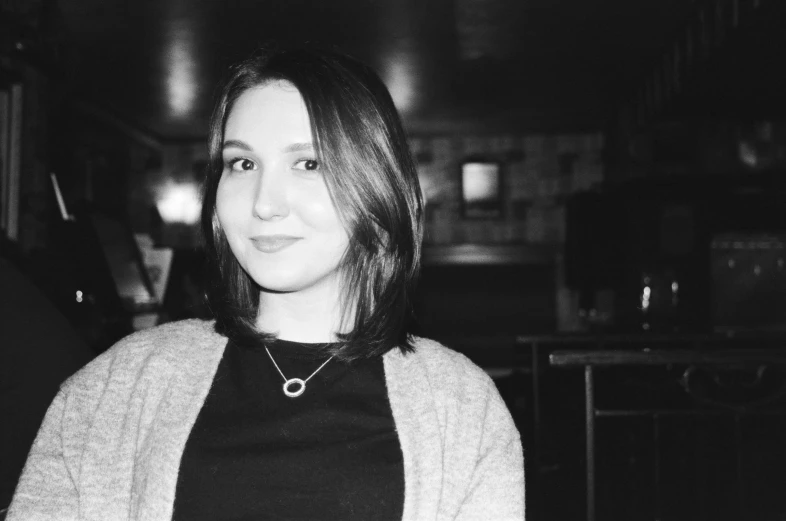 a black and white photo of a woman sitting at a table, a black and white photo, unsplash, realism, in a pub, halfbody headshot, around 1 9 years old, slightly colorful