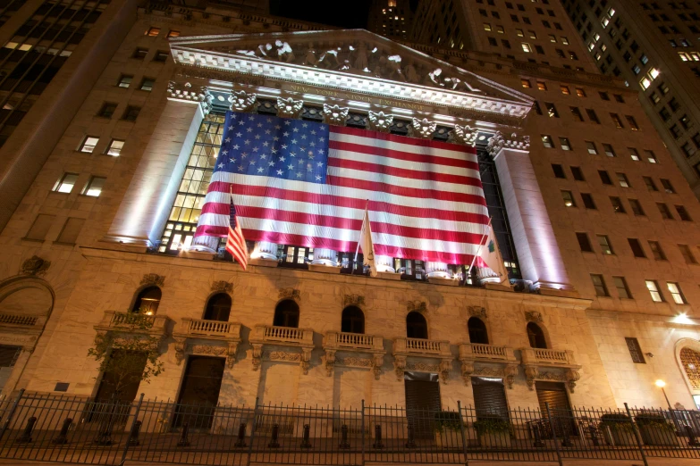 a large american flag hanging from the side of a building, trading stocks, square, during the night, markets