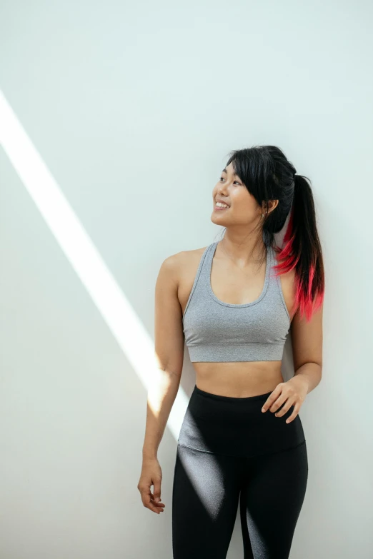 a woman in a gray top and black leggings, inspired by helen huang, pexels contest winner, sports bra, turning her head and smiling, in front of white back drop, bright daylight indoor photo