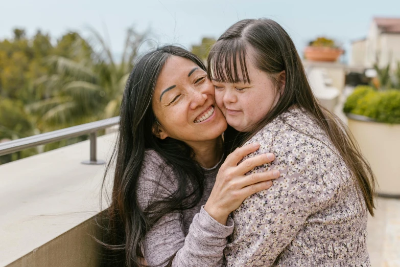 two women hugging each other on a balcony, trending on pexels, hurufiyya, andy milonakis, in australia, joy ang, woman with braided brown hair