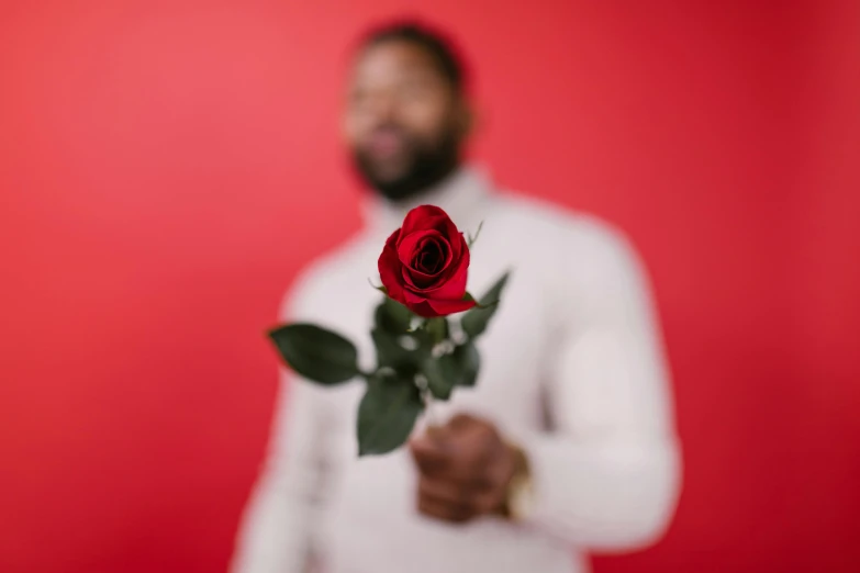 a man in a white shirt holding a red rose, by James Warhola, pexels contest winner, man is with black skin, in red background, instagram post, flowers in background