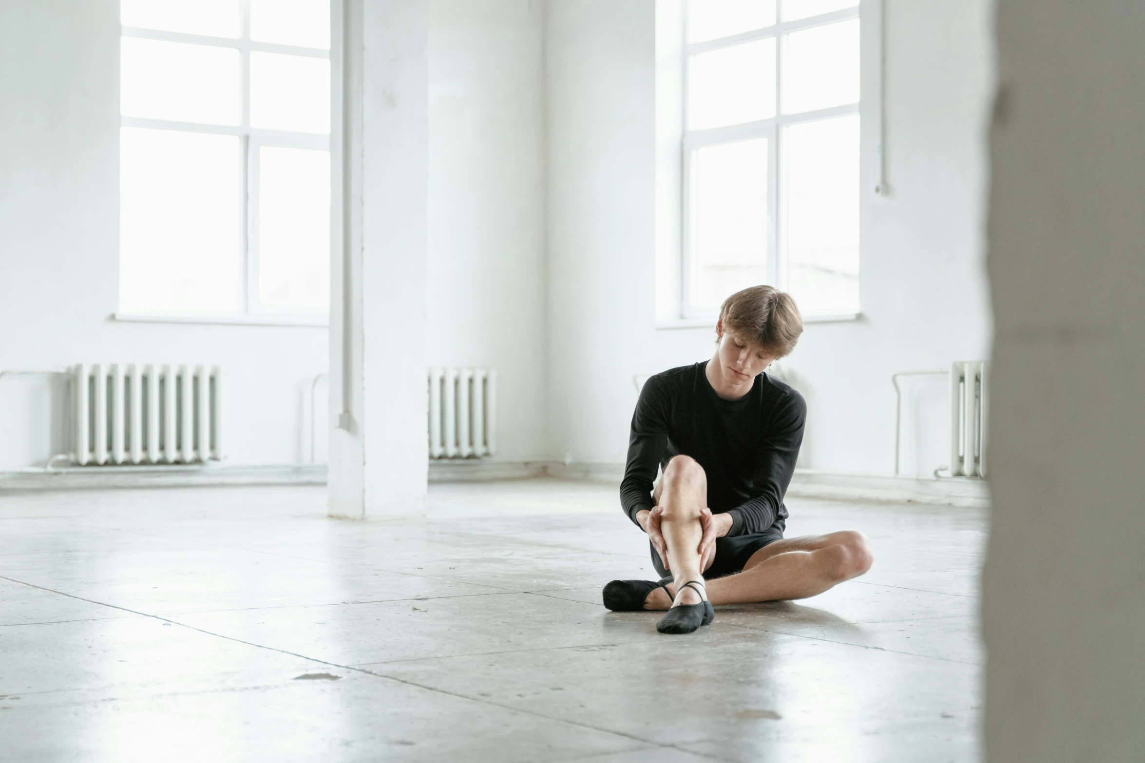 a woman sitting on the floor in a room, by Nina Hamnett, unsplash, thin young male, pointe poses, ukrainian, ignant