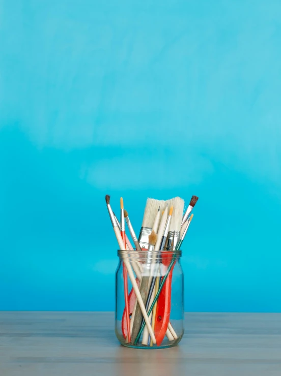 a jar filled with paint brushes on top of a wooden table, a photorealistic painting, pexels, cyan photographic backdrop, 15081959 21121991 01012000 4k, ilustration, no text!