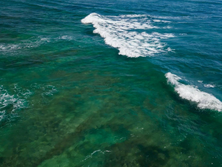 a person riding a surfboard on a wave in the ocean, blue and green water, manly, aerial, coral reef