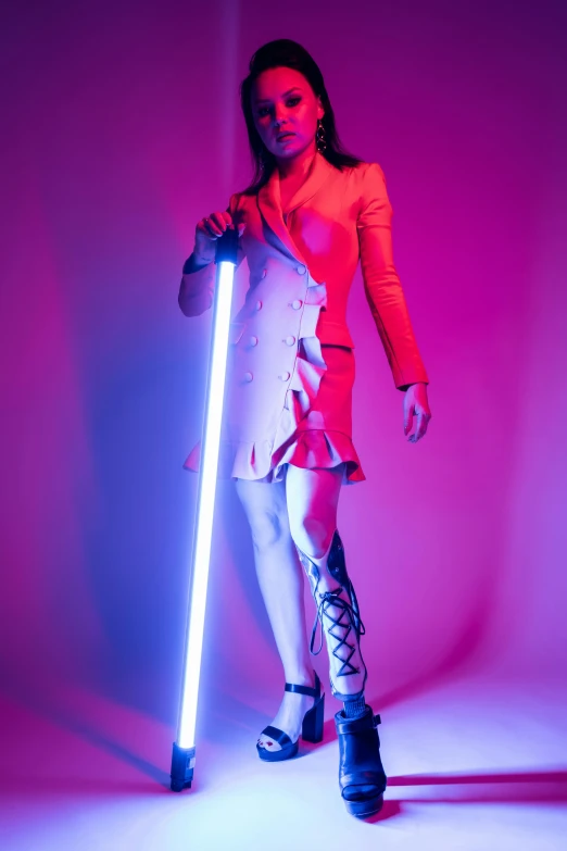 a woman holding a light saber in front of a pink background, inspired by hajime sorayama, blue and orange lighting, cybernetic legs, photograph taken in 2 0 2 0, with a walking cane