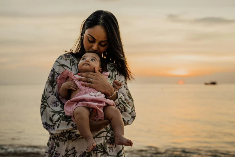 a woman holding a baby on the beach, a portrait, pexels contest winner, manuka, pink golden hour, an olive skinned, 1 2 9 7