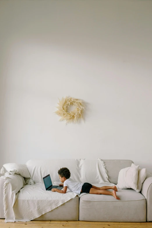 a person laying on a couch with a laptop, by Carey Morris, pexels contest winner, interior white wall, kids playing, clean and simple design, decoration around the room