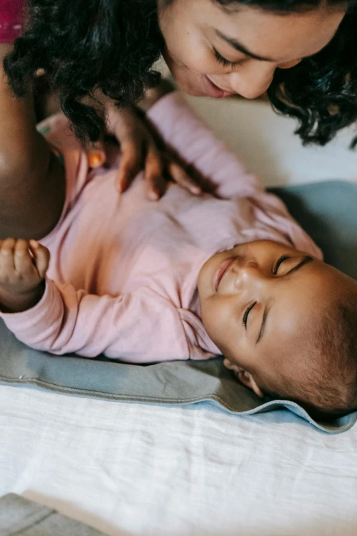 a woman holding a baby on top of a bed, by Nina Hamnett, trending on unsplash, soft pads, laying down, ebony, zoomed in