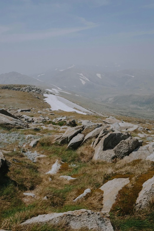 a man standing on top of a rocky hill, les nabis, snowy mountains, hazy and dreary, stone paths, rocky grass field