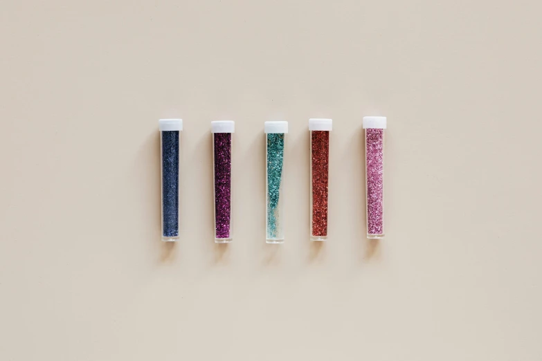 three tubes filled with glitter sitting on top of a table, 5 colors, gravels around, minimal palette, swarovski crystals