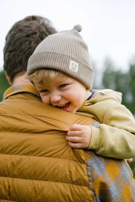 a man holding a small child in his arms, pexels, hat and hoodie, model wears a puffer jacket, birch, two men hugging