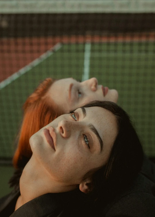 a couple of people laying on top of a tennis court, inspired by Elsa Bleda, trending on pexels, realism, woman with red hair, beautiful gemini twins portrait, proud looking away, pictured from the shoulders up