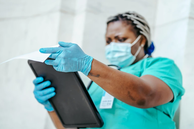 a woman in a green shirt and blue gloves holding a tablet, by Meredith Dillman, pexels contest winner, nurse scrubs, ap photo, thumbnail, black