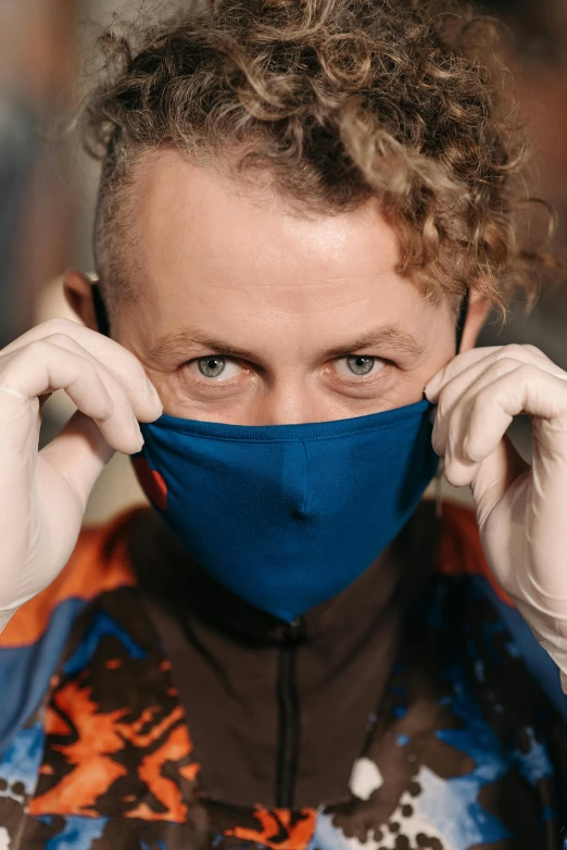 a close up of a person wearing a face mask, inspired by Jan Asselijn, paulie shore, blue and orange, wearing gloves, blue-eyed man