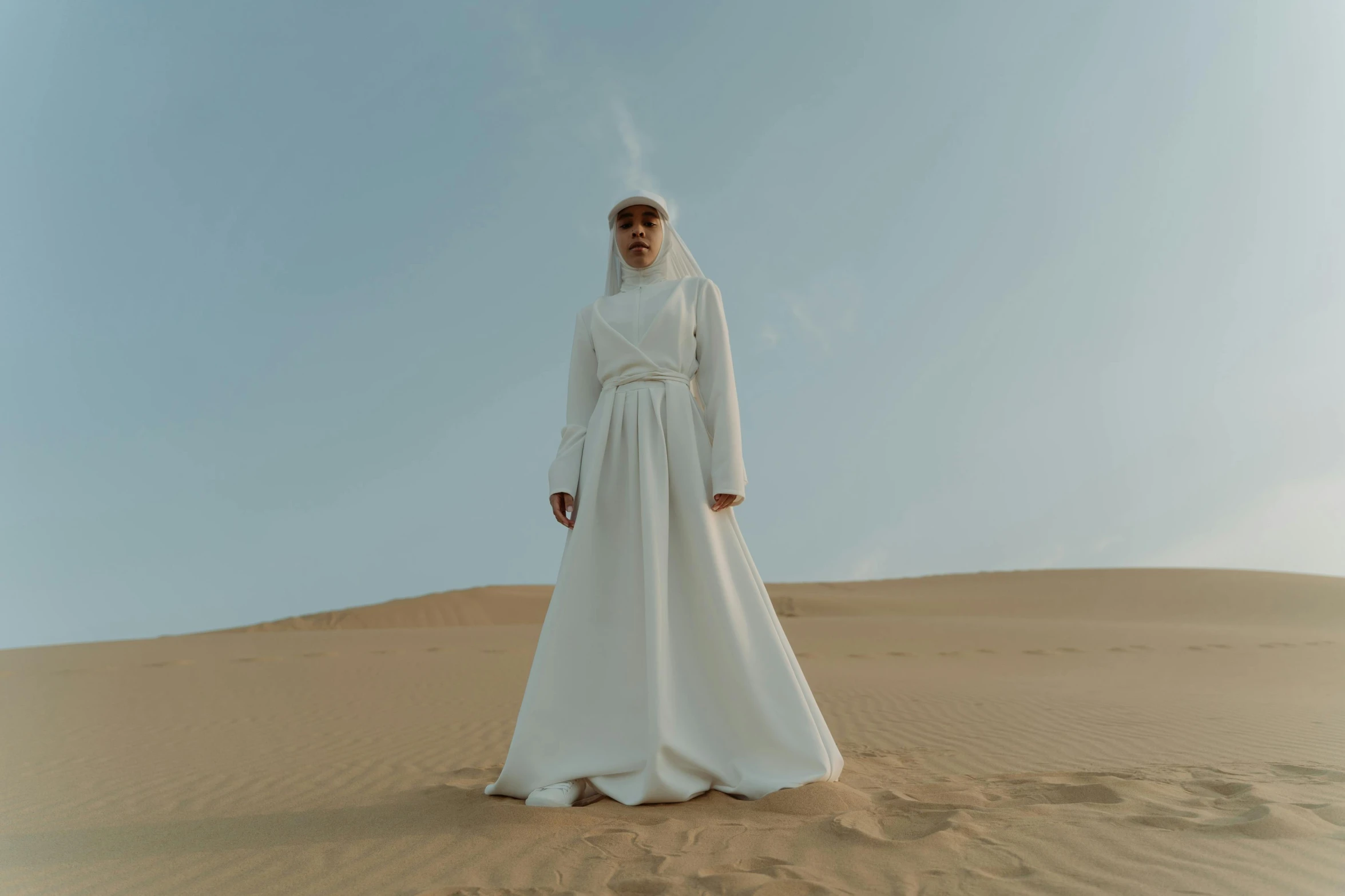 a man standing in the middle of a desert, an album cover, inspired by Modest Urgell, pexels contest winner, hurufiyya, nico wearing a white dress, nun fashion model, ( ( theatrical ) ), white hijab