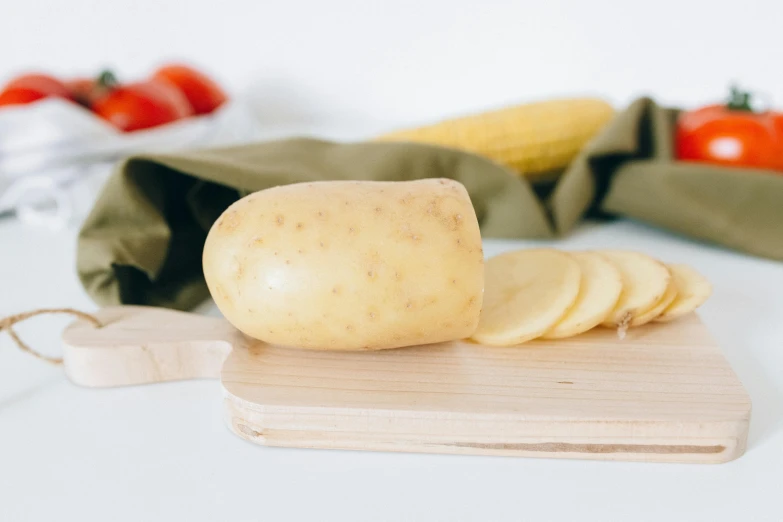 a potato sitting on top of a wooden cutting board, a picture, unsplash, with a white background, various posed, corn, soft shade