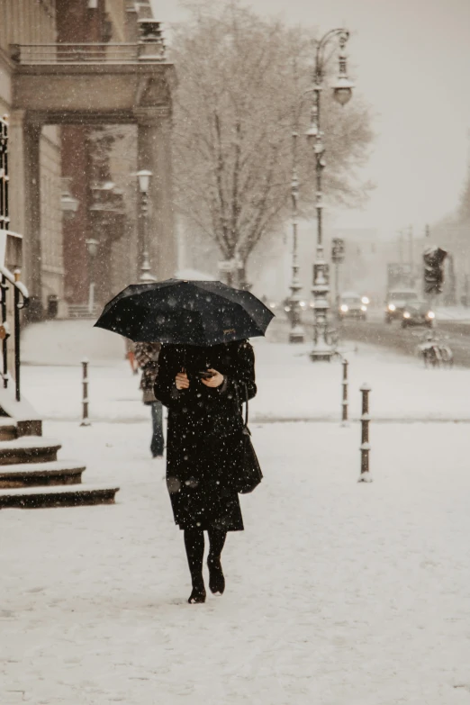 a woman walking in the snow with an umbrella, pexels contest winner, black overcoat, hannover, covered!, trending on