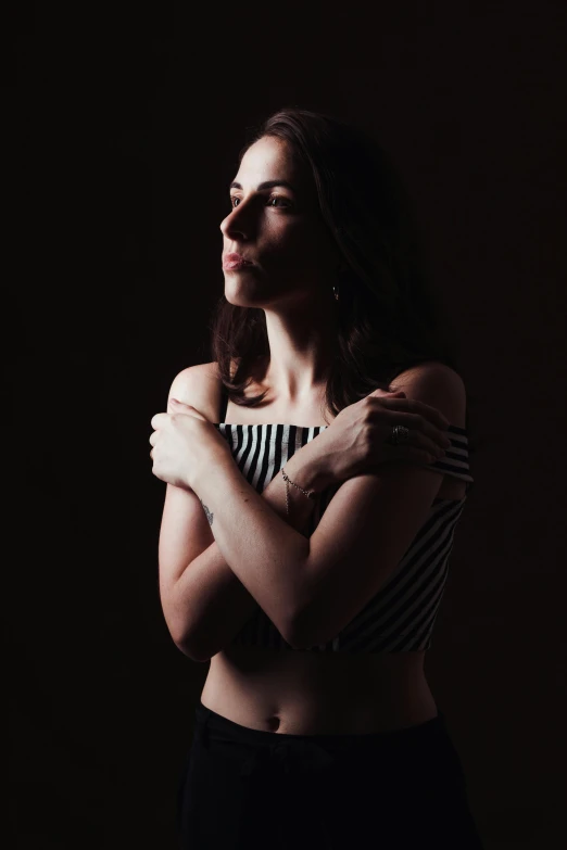 a woman standing in the dark with her arms crossed, a black and white photo, inspired by Elsa Bleda, unsplash, wearing a crop top, alison brie, album cover, studio lit