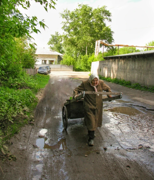 a man carrying a piece of luggage down a muddy road, by Ilya Ostroukhov, pexels contest winner, socialist realism, filling with water, an old lady, 15081959 21121991 01012000 4k, pouring