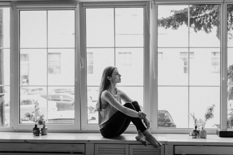 a black and white photo of a woman sitting on a window sill, a black and white photo, satisfied pose, in style of britt marling, ballerina, wide windows