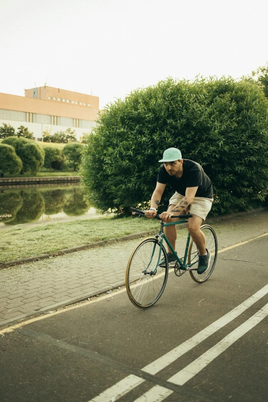 a man riding a bike down a street next to a body of water, a picture, green spaces, melbourne, half length, item