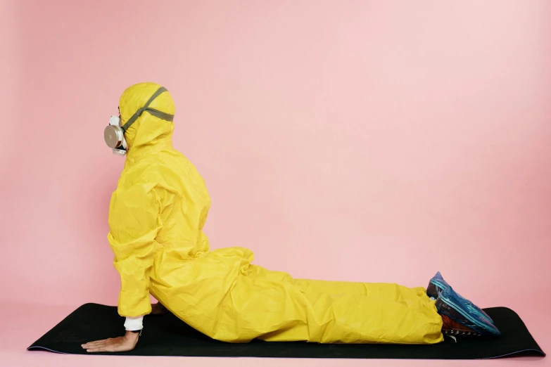 a person in a yellow suit sitting on a black mat, inspired by Sarah Lucas, unsplash, plasticien, surgical gown and scrubs on, pink and yellow, dynamic stretching, biohazard