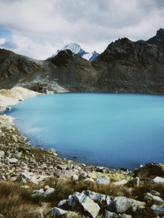 a body of water surrounded by rocks and grass, a colorized photo, hurufiyya, andes, fan favorite, lake blue, peruvian looking