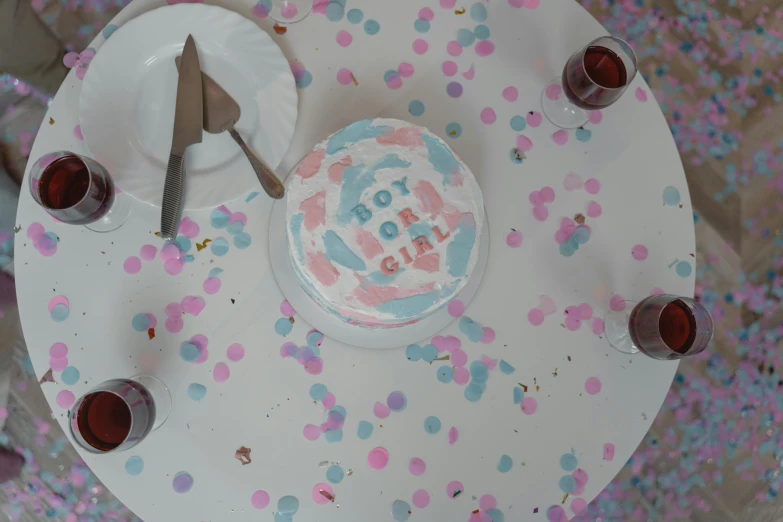 a cake sitting on top of a table covered in confetti, by Arabella Rankin, process art, pregnancy, pink and blue colour, high - angle view, promo image