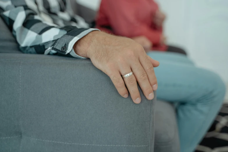 a close up of a person sitting on a couch with a ring on their finger, adult man, grey and silver, distant - mid - shot, silver，ivory